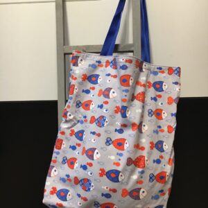 Stofftasche mit buntem Fisch-Print und blauen Henkeln an einer Leiter