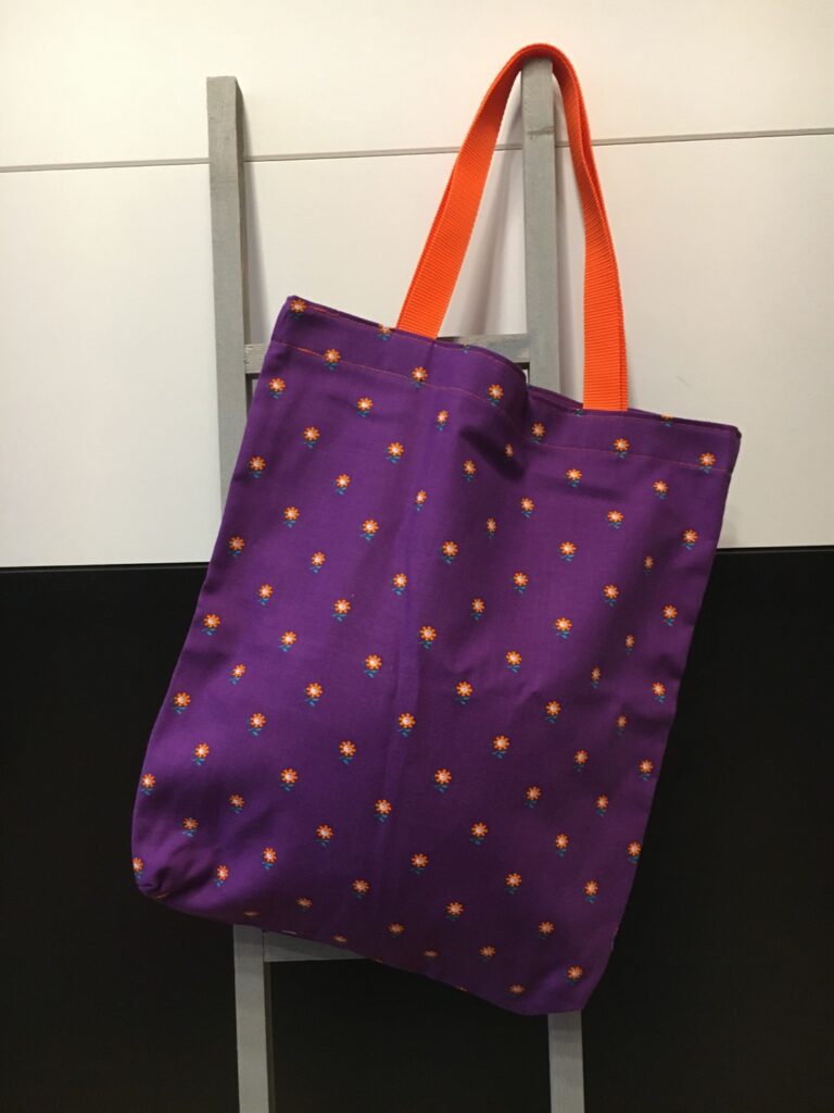 Stofftasche in Lila mit kleinem Blütenmuster und orangen Henkeln