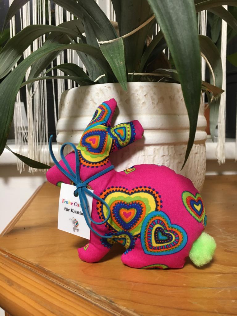Buntes Stoffhäschen mit Regenbogen- und Herzmuster auf Holzboden