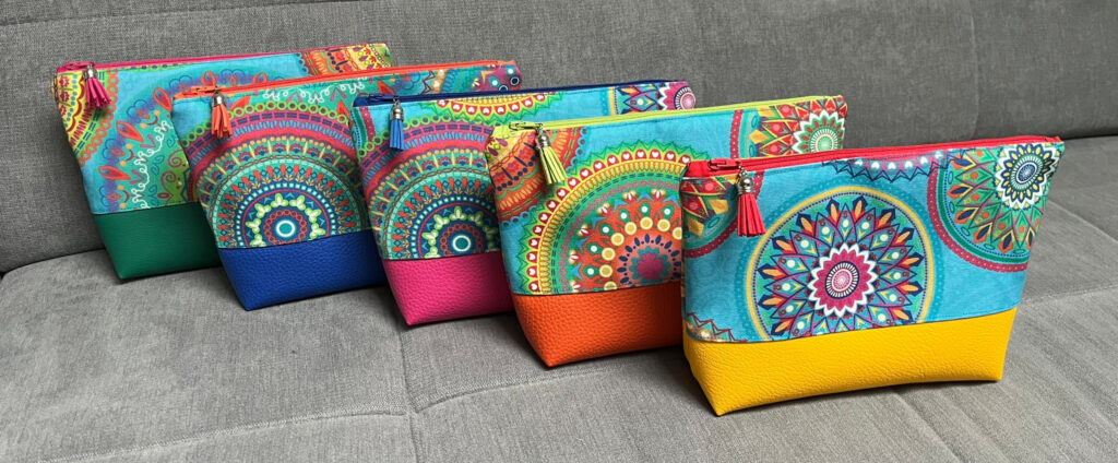 Fünf Kosmetiktaschen mit Mandalamuster und farbigem Kunstlederboden auf grauem Sofa