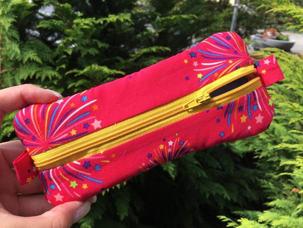Kosmetikbeutel in Pink mit buntem Print und gelbem Reißverschluss im Garten