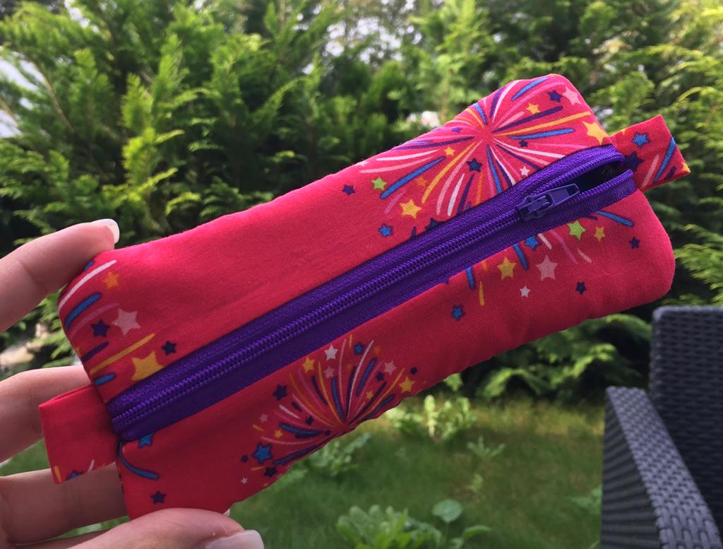 Kosmetikbeutel in Pink mit buntem Print und violettem Reißverschluss im Garten
