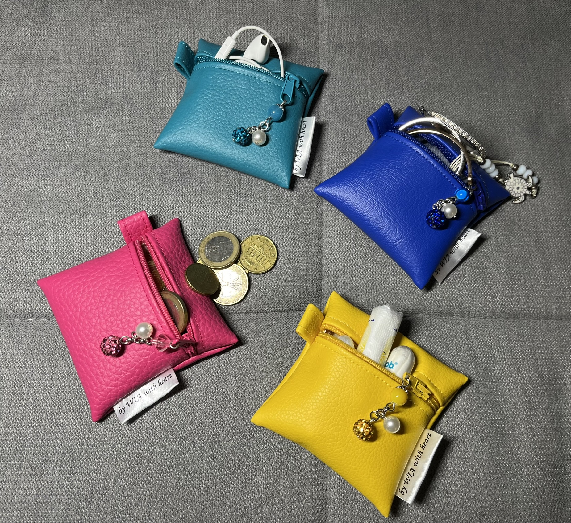 Vier Kunstledertäschchen in Türkis, Blau, Pink und Gelb mit Perlenanhängern und Inhalt