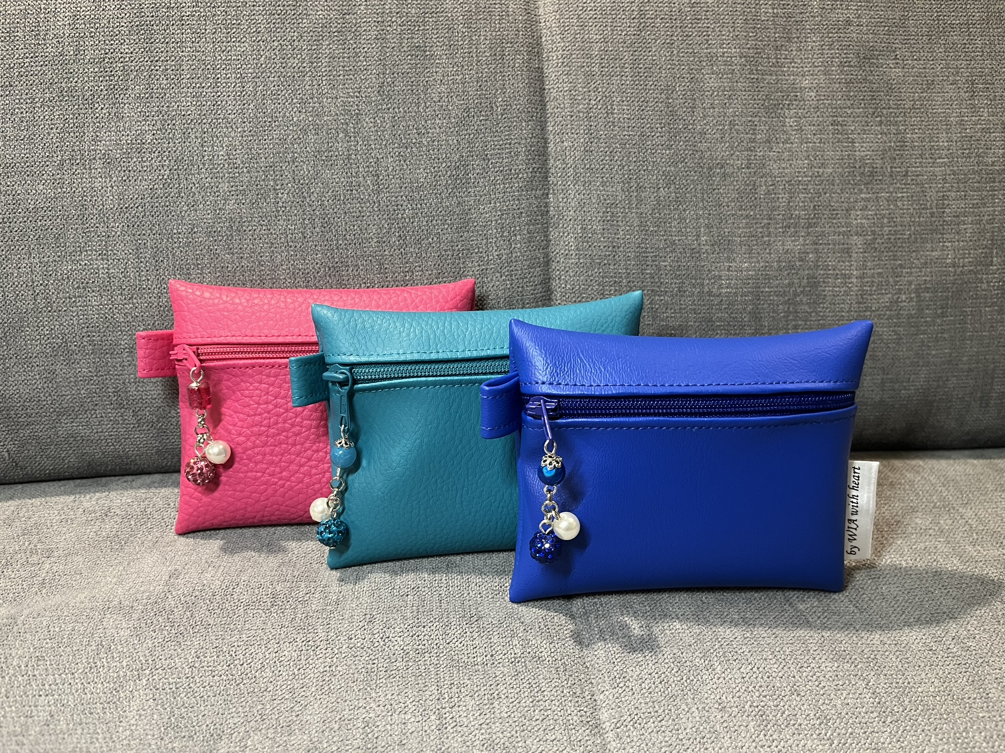 Drei Kunstledertäschchen in Pink, Türkis und Blau mit Perlenanhängern auf dem Sofa