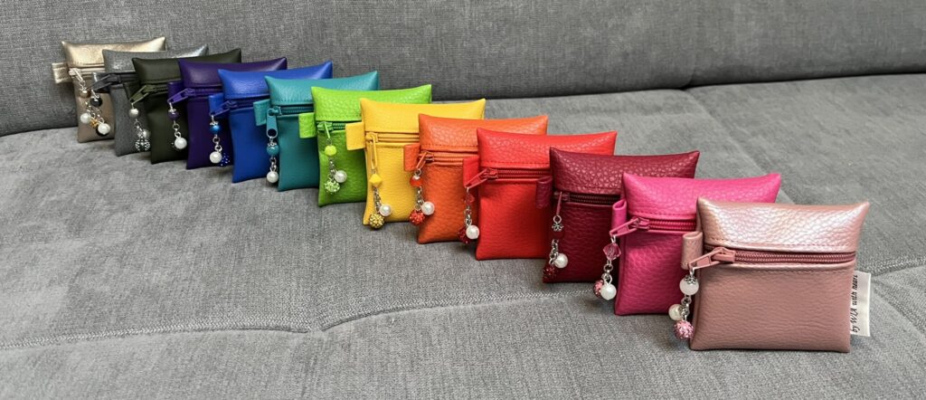 Reihe bunter Kunstledertäschchen mit Perlenanhängern auf grauem Sofa