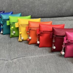 Reihe bunter Kunstledertäschchen mit Perlenanhängern auf grauem Sofa